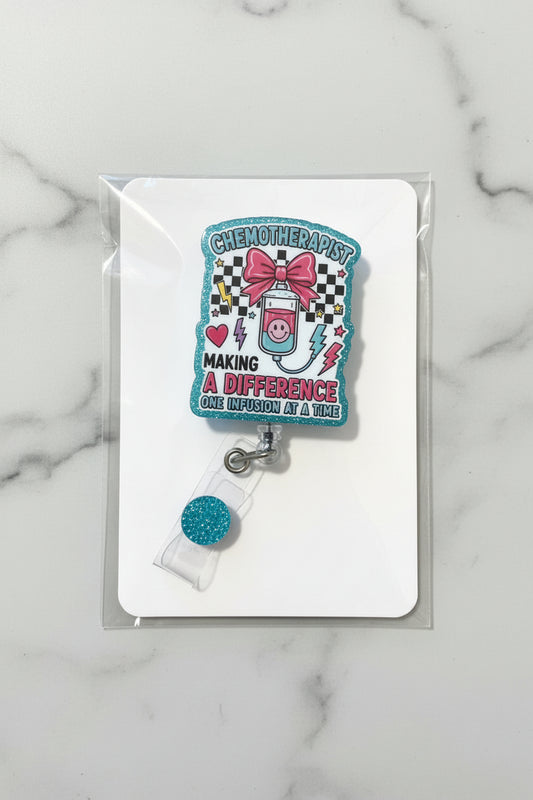A chemotherapy-themed acrylic keychain or badge holder attached to a clear plastic clip with a blue glitter round charm, displayed on a white backing card over a gold glitter background.